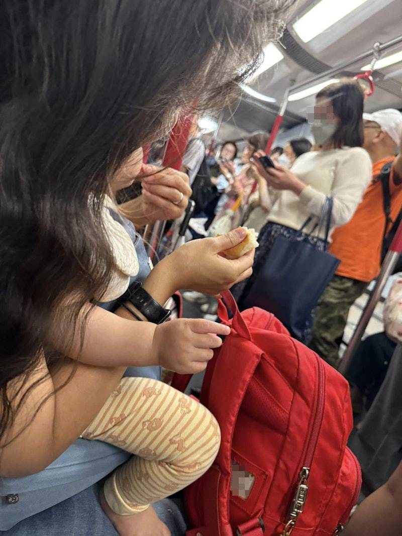 麵包 1名媽媽坐在港鐵車廂內座位上,BB坐在她的腿上,媽媽一手拿著麵包,另一手撕下小塊麵包餵BB食。(圖片來源:FB@將軍澳主場)